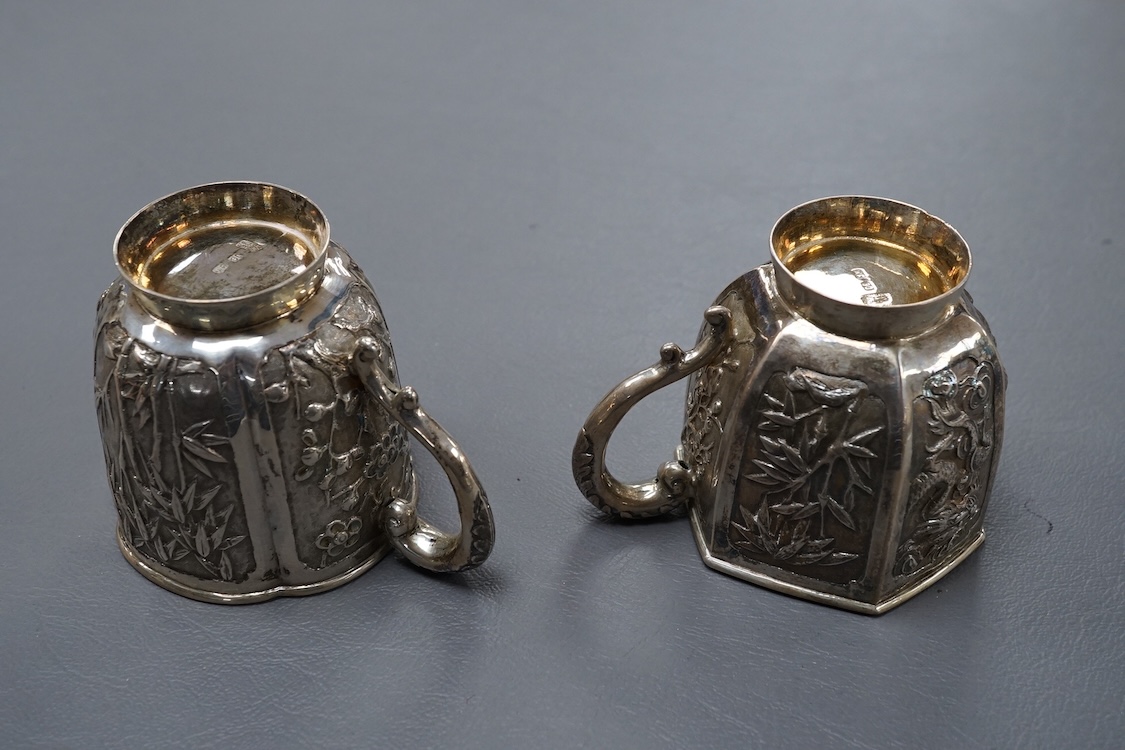 Two late 19th/early 20th century Chinese Export white metal tea cups, maker Wing Fat, embossed with bamboo, chrysanthemums and figures, of hexagonal or cusped form, 5.4oz.